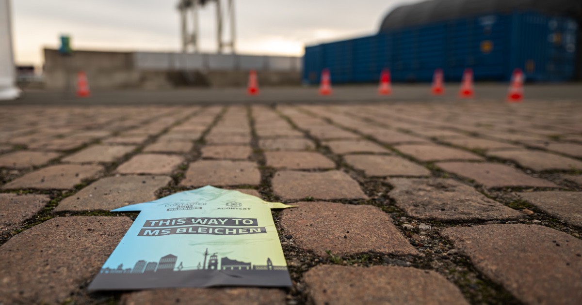 Directional sign on cobblestones reading \"This Way to MS Bleichen\" with the ContainerDays Hamburg 2026 logo, guiding attendees to the venue at the harbor